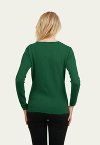 Pull vert à manches longues avec col rond ; fabriqué en tissu doux ; design ajusté mettant en avant le dos et la longueur des bras. Associé avec un pantalon noir.