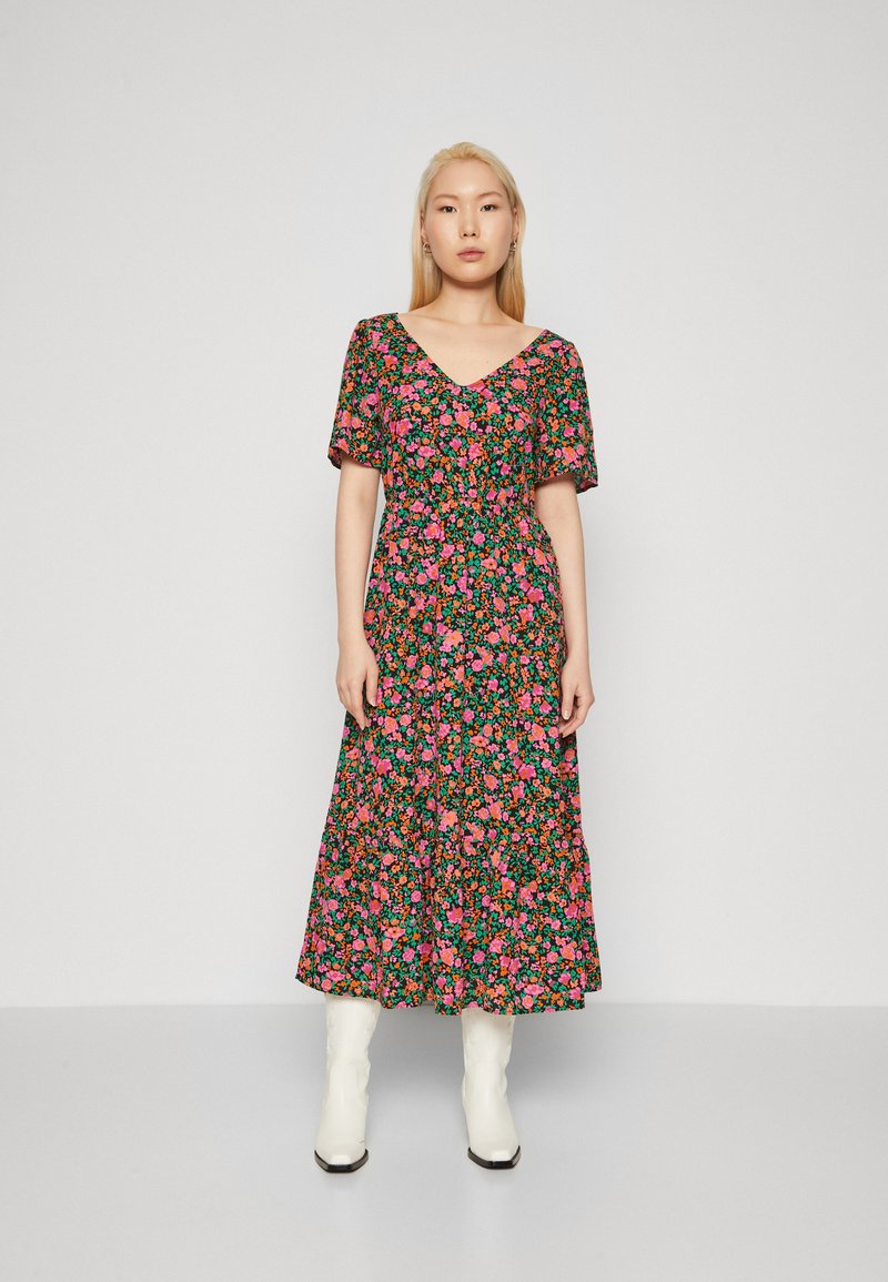 Robe à fleurs avec un fond noir et des fleurs colorées roses et vertes, décolleté en V, manches courtes et longueur midi fluide.