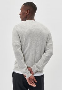 Svijetlosivi pulover od mekanog materijala, s okruglim izrezom i dugim rukavima, s rebrastim manžetama i rubom. Detaljno šivenje na donjem dijelu.