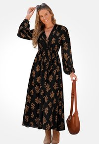 Černé květinové maxi šaty s dlouhými rukávy, s výstřihem do V, úzkým pasem a hnědými květinovými vzory. Spárováno s béžovými kotníkovými botami a hnědou taškou.