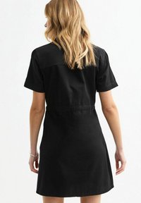 Black short-sleeved dress with a fitted waist, soft fabric, and a straight silhouette. Includes a centered back seam and no visible patterns.