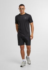 Svart atletisk t-skjorte med korte ermer, kombinert med svarte shorts. Antrekket har en diskret logo og er komplementert av sølvfargede joggesko.