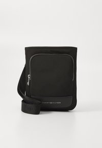 Černá nylonová taška přes rameno s přední kapsou na zip, vybavená texturovaným panelem a tkaným popruhem, s logem "TOMMY HILFIGER".