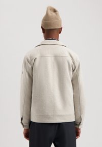 Light grey wool-blend jacket with a wide collar, flap pockets, and buttoned cuffs. Paired with a beige knitted beanie. Back view.