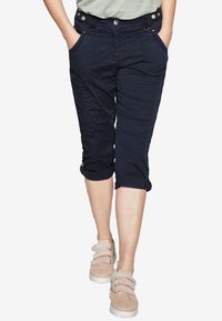 Pantalons cropped navy en tissu texturé, avec des poches avant et des ourlets retroussés, associés à des chaussures légères.