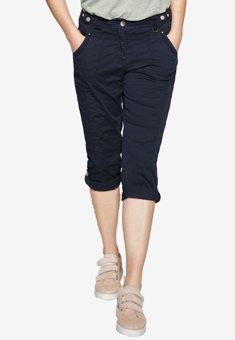 Pantalons cropped navy en tissu texturé, avec des poches avant et des ourlets retroussés, associés à des chaussures légères.