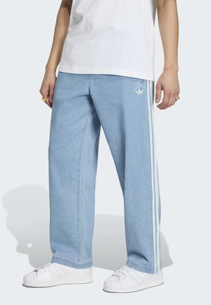 Osoba nosi Adidas svijetloplave široke trenirke s bijelim prugama, bijele Adidas tenisice i bijelu majicu.