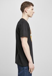 Svart bomull t-skjorte med korte ermer, med et fargerikt grafisk trykk på framsiden. Passformen er vanlig, som passer til blå denim jeans.