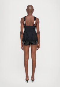 Top negro sin mangas con tirantes ajustables y herrajes plateados, combinado con pantalones cortos negros brillantes. Tejido suave, forma estructurada y silueta de bolsa.