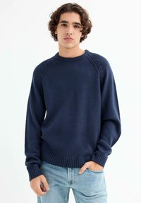 Suéter de lana de color azul marino con cuello redondo, puños y dobladillo acanalados, que presenta un diseño texturizado a lo largo de las mangas raglán.