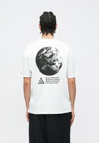 Λευκό T-shirt με κοντά μανίκια, με μεγάλο μαύρο γραφικό της Γης στην πλάτη και κείμενο. Casual εφαρμογή, κατασκευασμένο από απαλό βαμβακερό ύφασμα.