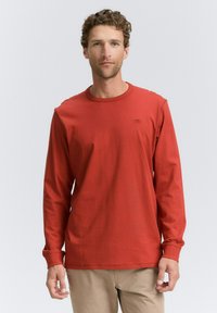 Langärmliges rotes T-Shirt aus Baumwolle mit Rundhalsausschnitt und umgeschlagenen Ärmeln, versehen mit einem kleinen Logo auf der Brust.
