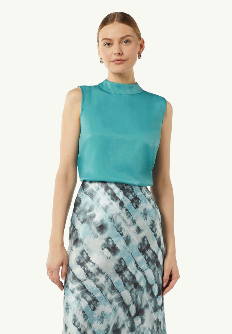 Türkiser ärmelloser Oberteil mit hohem Kragen, kombiniert mit einem gemusterten Rock, der blaue und schwarze abstrakte Designs aufweist. Stoff ähnlich Seide.