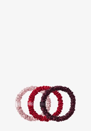 Tres coleteros elásticos cubiertos de satén en rosa claro, rojo y púrpura oscuro, cada uno con una pequeña etiqueta que dice "slip."