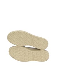 Suole di scarpe in gomma di un beige chiaro con un motivo esagonale, dotate di impugnature testurizzate e di un piccolo logo del marchio impressa su una suola.
