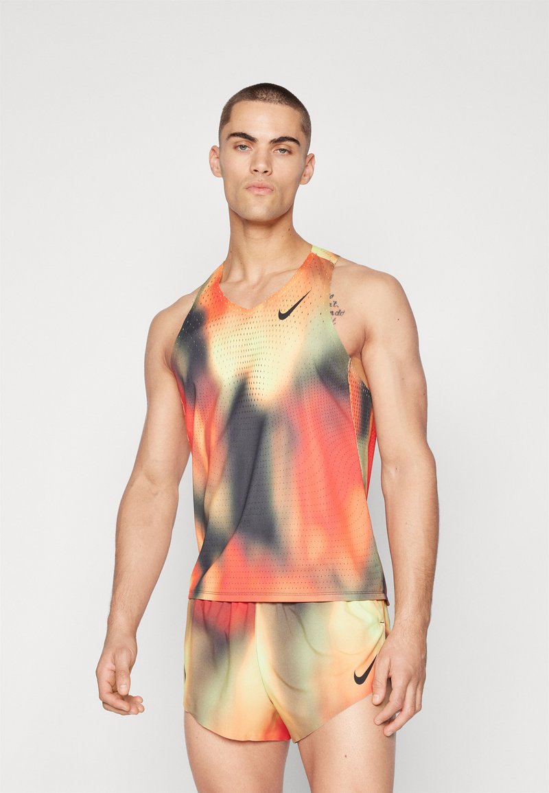 Orange und schwarzes, gemustertes Sporttanktop mit V-Ausschnitt und perforierter Textur, kombiniert mit passenden Shorts, die ein schwarzes Logo tragen.