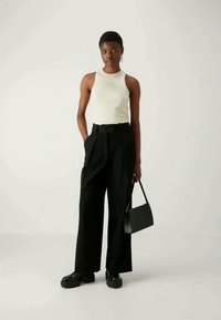 Krēmveida bezpiedurkņu topi, melnas plaša kāju bikses, melna rokas soma un masīvas melnas kurpes. Vienkārša dizaina ar tīrām līnijām un bez redzamām rakstu zīmēm.