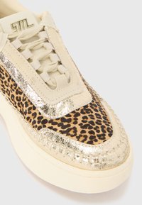 Sneaker with a leopard print fabric upper and metallic gold accents, featuring a textured beige rubber sole and flat beige laces.