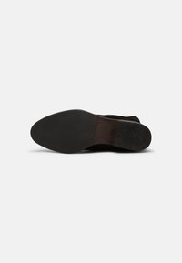 Semelle de chaussure noire pour homme avec avant texturé, milieu lisse et petit talon sur fond blanc.
