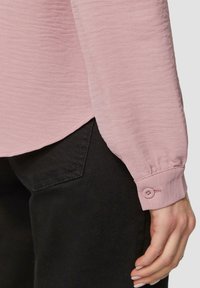 Helles rosa Langarmshirt aus strukturiertem Stoff mit einem knöpfbaren Bündchen, kombiniert mit schwarzen Hosen mit Taschen-Detail.