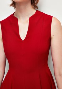 Czerwona sukienka bez rękawów z dekoltem w kształcie litery V, dopasowanym górnym partem i rozkloszowanym dołem. Gładki, jednolity materiał z pionowymi szwami. Prosty, elegancki design.