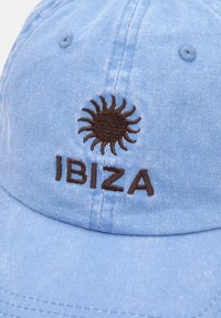 Light blue cotton cap with a curved brim; features brown embroidered sun and "IBIZA" text on the front. Textured, casual design.
