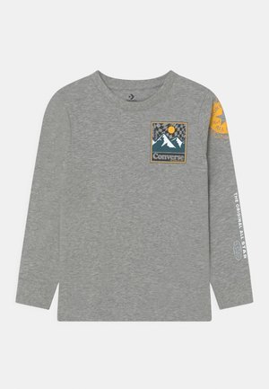 Szara koszulka Converse z długim rękawem z naszywką przedstawiającą górę i słońce na piersi, żółte okrągłe logo na prawym ramieniu oraz biały tekst na lewym rękawie.