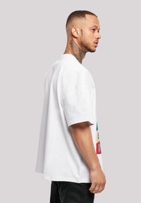 Hvit oversized t-skjorte med korte ermer, med et fargerikt grafisk trykk på forsiden, vist fra siden mot en nøytral bakgrunn.
