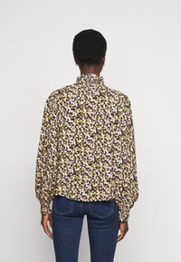 Vloeiende zwarte blouse met een klein roze en gele bloemenpatroon, verzamelde hoge kraag en volumineuze lange mouwen. Gepaarde met blauwe denim.