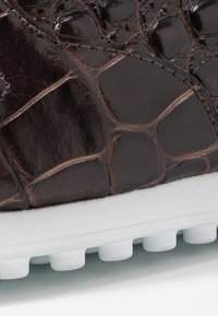 Baskets en cuir marron avec une texture gaufrée crocodile, semelle en caoutchouc blanche et détails de broderie discrets. Accent sur le design de la surface supérieure.