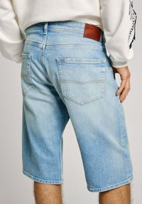 Pantalones cortos de mezclilla azul claro con un corte relajado, que cuentan con dos bolsillos traseros, un parche de cuero marrón y mínimos acentos de costura.