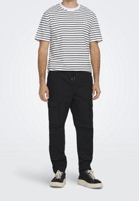 Stribet kortærmet t-shirt i hvid og sort, parret med sorte cargo-bukser med sidelommer og sorte sneakers med hvide såler.