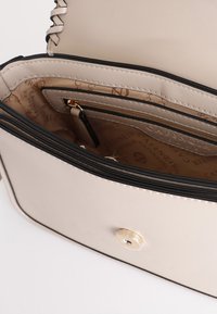 Beige syntetisk handväska med svarta detaljer, som har ett organiserat inre, zipficka och guldhardware. Slät textur och minimalistisk design.