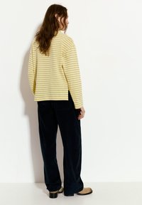 Pullover giallo a righe con vestibilità comoda, abbinato a pantaloni in velluto a coste navy a gamba larga e stivali senza tacco beige con tacco nero.