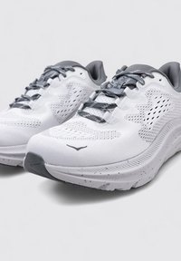 Scarpe sportive bianche con un upper in rete texturizzata, accenti grigi e suola maculata. Presentano un collare imbottito e lacci a fantasia.