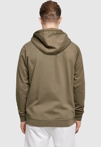 Olivgrön hoodie med dragsko i huven, ribbade ärmslut och nederkant. Mjuk tygtextur, sedd bakifrån, utan grafiska element eller mönster.