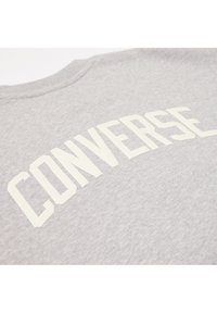 Sudadera gris con gran texto blanco "CONVERSE" en el pecho. El material parece suave y tiene una textura lisa. Diseño clásico de cuello redondo.
