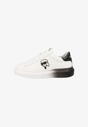 Witte sneaker met zwarte gradaties zool, zwarte hieltab, en een cartoongezicht met zonnebril aan de zijkant.