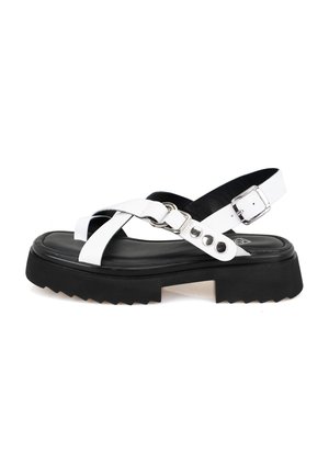Sandales blanches avec une semelle noire épaisse, dotées de brides croisées, d'une fermeture à boucle et de détails en métal argenté. Semelle rayée pour une meilleure adhérence.