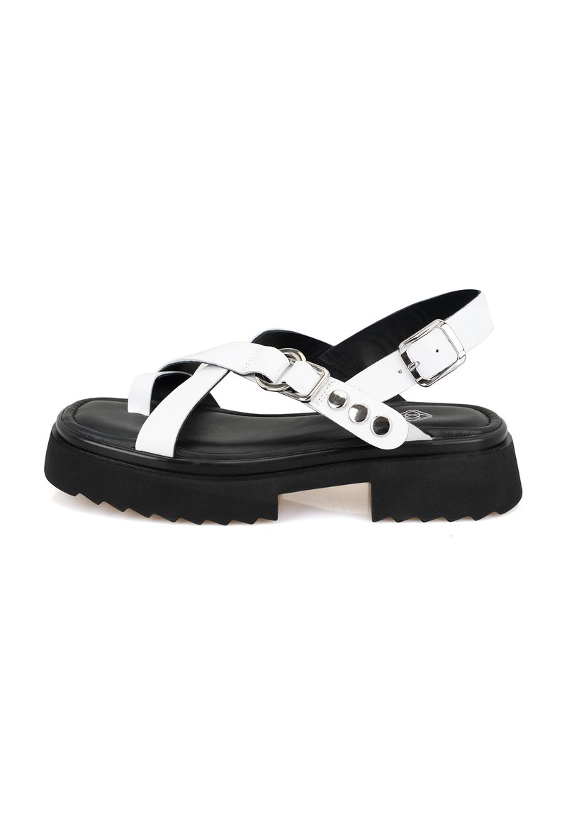 Witte sandalen met een stevige zwarte zool, voorzien van kruistraps, een gespafsluiting en zilveren hardware details. Geribbelde zool voor grip.