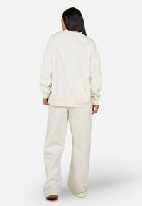 Felpa oversize color crema con polsini e orlo a costine, abbinata a pantaloni a gamba larga coordinati, entrambi in un tessuto morbido.