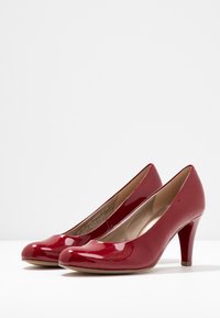 Tacchi alti in pelle verniciata rossa con punta arrotondata e tacco a stiletto di 5 cm. Texture liscia e leggero lucido, presentano un design slip-on.