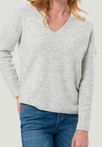 Pull en tricot gris clair avec un col en V, texture côtelée et manches longues, associé à un jean bleu.