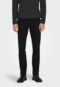 Jeans negros con un diseño ajustado, fabricados en tela de mezclilla. Combinados con un suéter oscuro texturizado y botas negras hasta el tobillo.