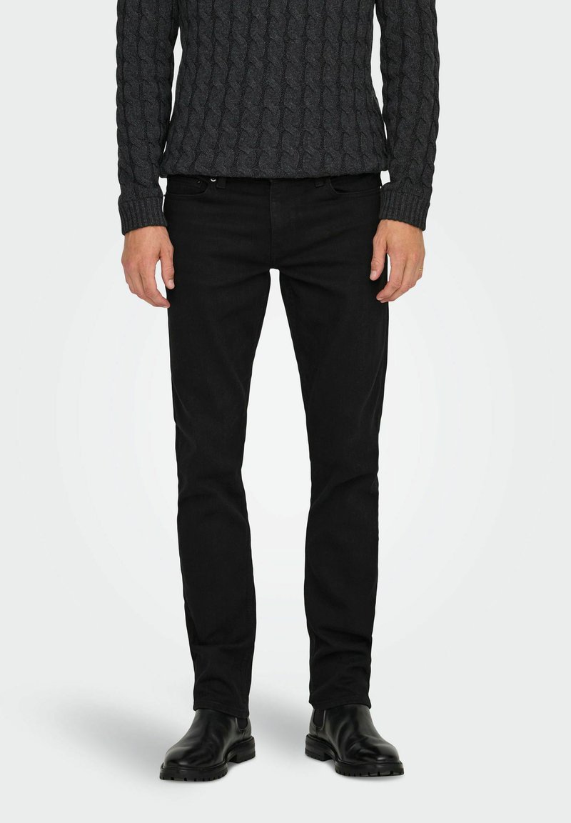 Jeans negros con un diseño ajustado, fabricados en tela de mezclilla. Combinados con un suéter oscuro texturizado y botas negras hasta el tobillo.
