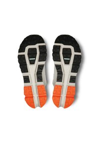 Chaussures de sport avec une semelle en caoutchouc noir et orange dotée de profondes rainures. La tige est gris clair avec des accents à motifs et une finition texturée.