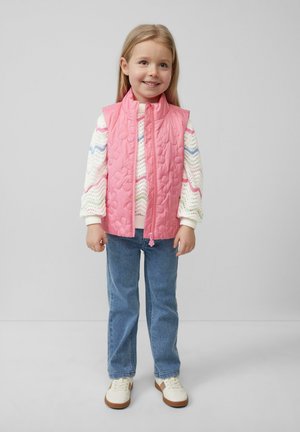 Gilet matelassé rose avec un col montant, porté sur un pull en laine multicolore blanc, associé à un jean bleu clair et des baskets crème.