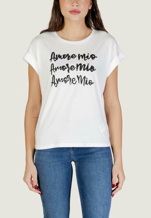 Donna che indossa una T-shirt bianca a maniche corte con la scritta "Amore Mio" ripetuta tre volte in corsivo nero, abbinata a jeans blu.