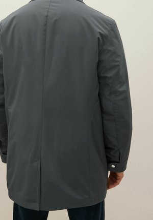 Tmavě šedý nepromokavý kabát se přímo střiženým střihem, viditelným prošitím a manžetami na knoflíky, s bočními kapsami a hladkou texturou.