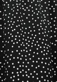 Μαύρο ύφασμα με μοτίβο από σκορπιστές μικρές λευκές πουά, με ελαφριές πτυχώσεις και υφή.